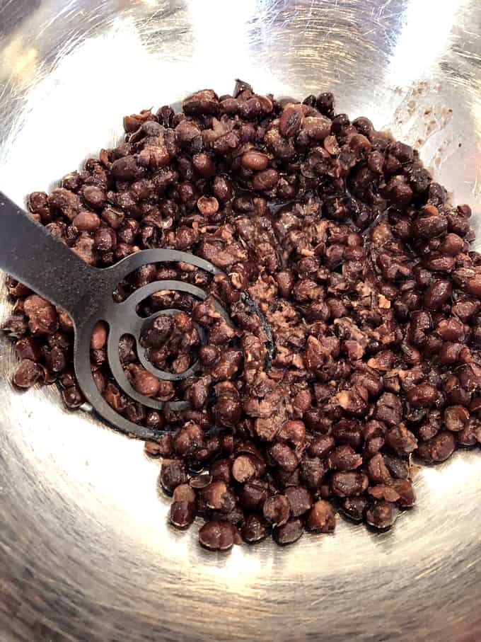 Mashing black beans with potato masher