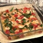 square clear oven safe baking dish filled with shrimp garnished with tomato, feta cheese and parsley