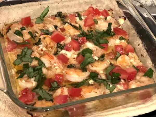 square clear oven safe baking dish filled with shrimp garnished with tomato, feta cheese and parsley