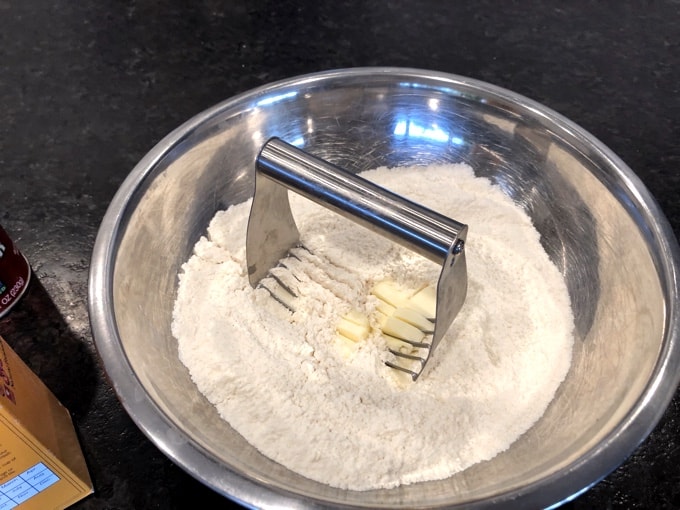 Using pastry blender to cut butter with flour in mixing bowl.