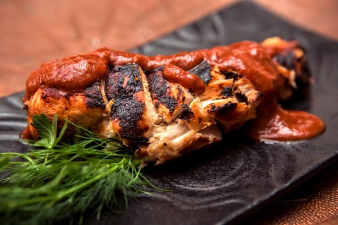 Baked BBQ Chicken Breast on black plate garnished with fresh herbs.