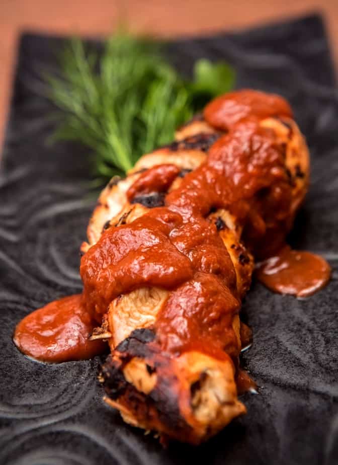 Baked Barbecue Chicken Breast on black plate with fresh herb garnish.