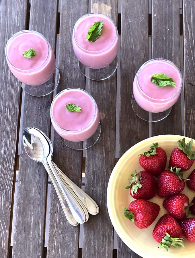 Strawberry mousse dessert glasses with fresh mint near plate of whole fresh strawberries.