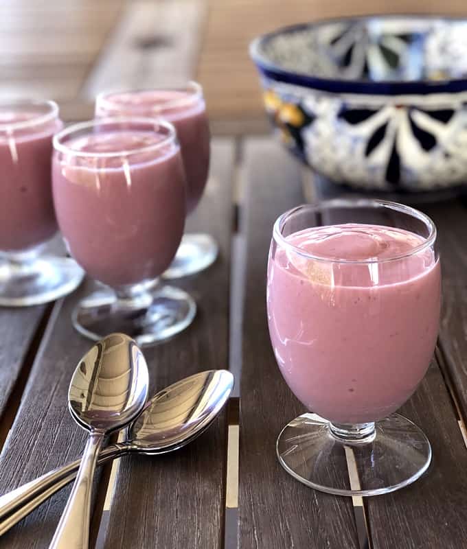 Creamy strawberry mousse in dessert glasses with spoons and decorative bowl in background.