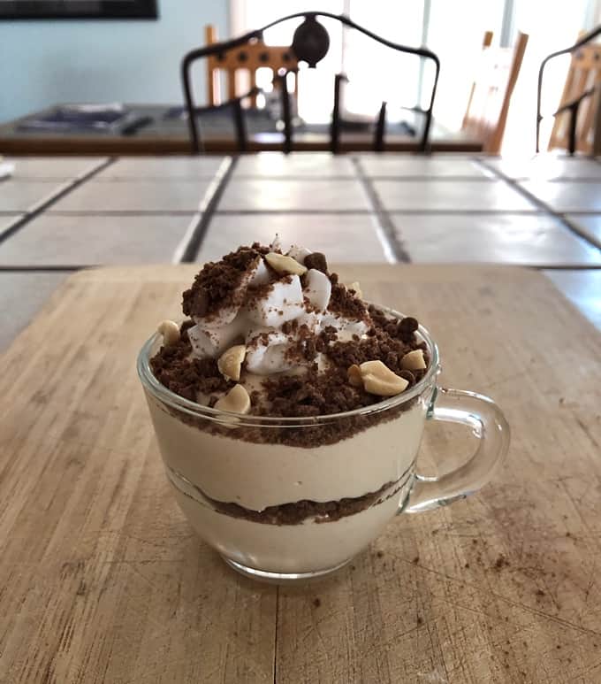 Chocolate peanut butter in a mug topped with lite whipped topping, crushed chocolate graham crackers and chopped peanuts.