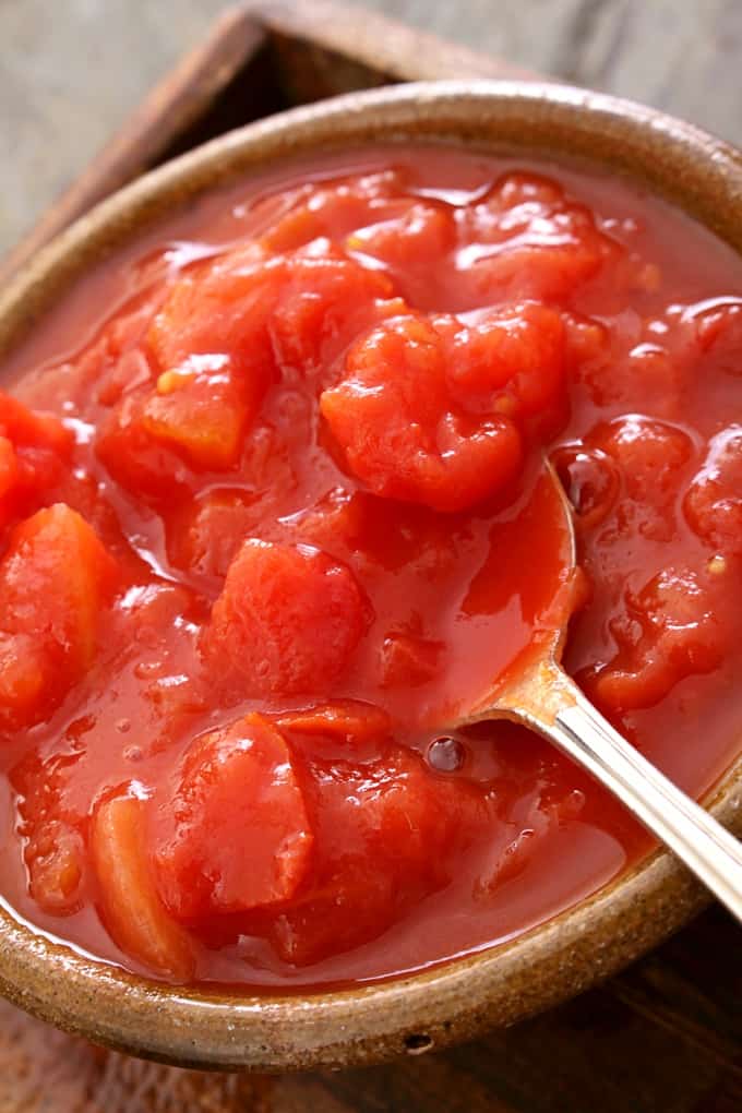 Chopped plum tomatoes in dish with large spoon.