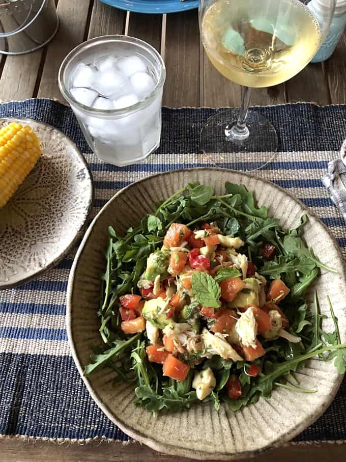 Crab and papaya salad with avocado on dinner plate with ear of corn on the cob, glass of ice water and glass of Chardonnay.