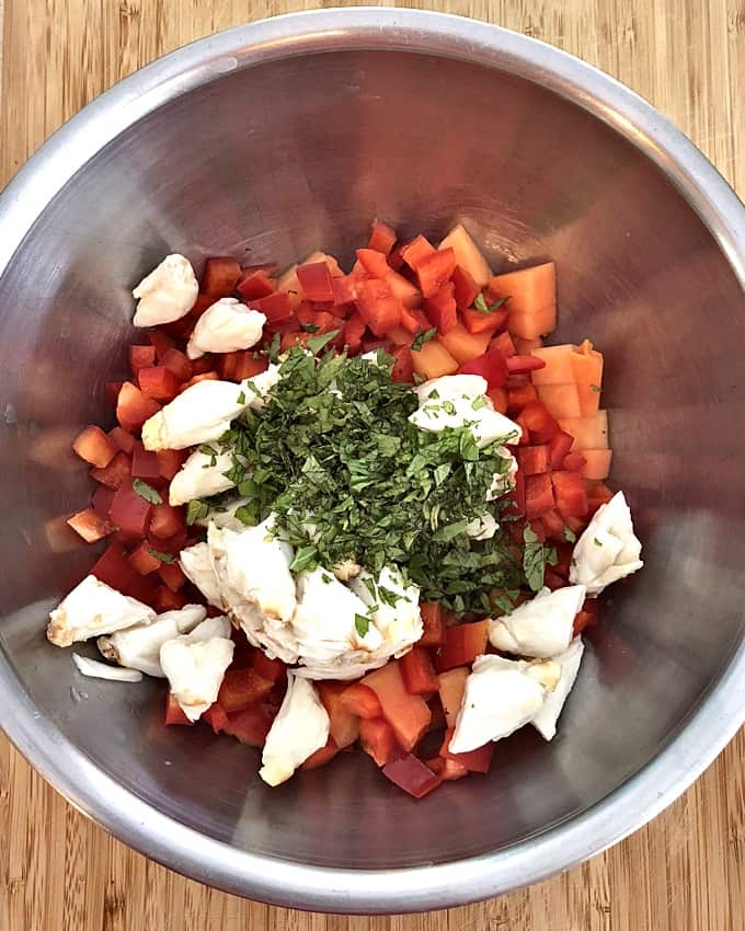 Adding crabmeat, papaya, bell pepper and mint to mixing bowl.