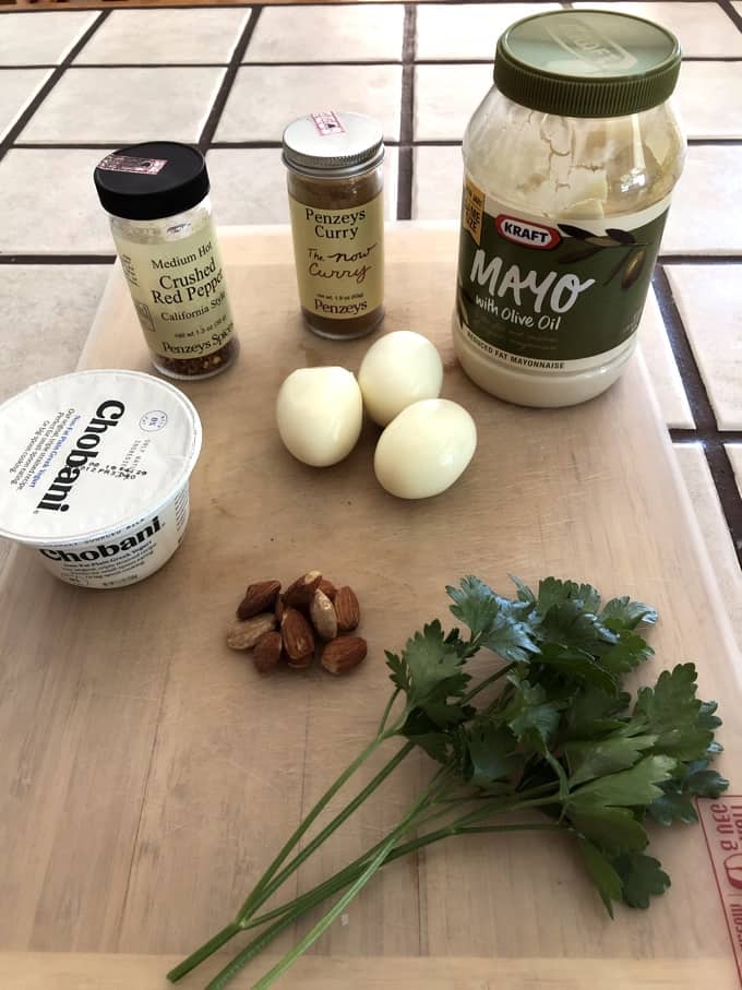 Ingredients for making curried egg salad including three hard boiled eggs, almonds, low fat mayonnaise, Greek yogurt, curry powder, crushed red pepper flakes and parsley.