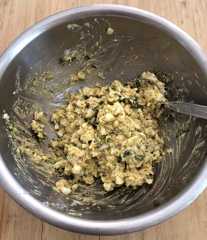 Curried egg salad in mixing bowl with spoon.