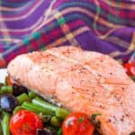 Baked salmon on white plate with tomatoes, olives and green beans.