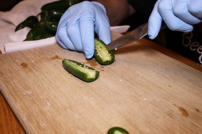 Seeding jalapeño chili pepper on wood cutting board while wearing blue kitchen gloves.
