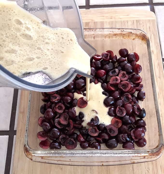 Pouring batter of fresh cherries in glass baking dish.
