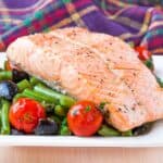 Salmon fillet on a bed of vegetables with colorful plaid napkins in the background