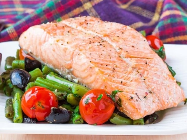 Salmon fillet on a bed of vegetables with colorful plaid napkins in the background