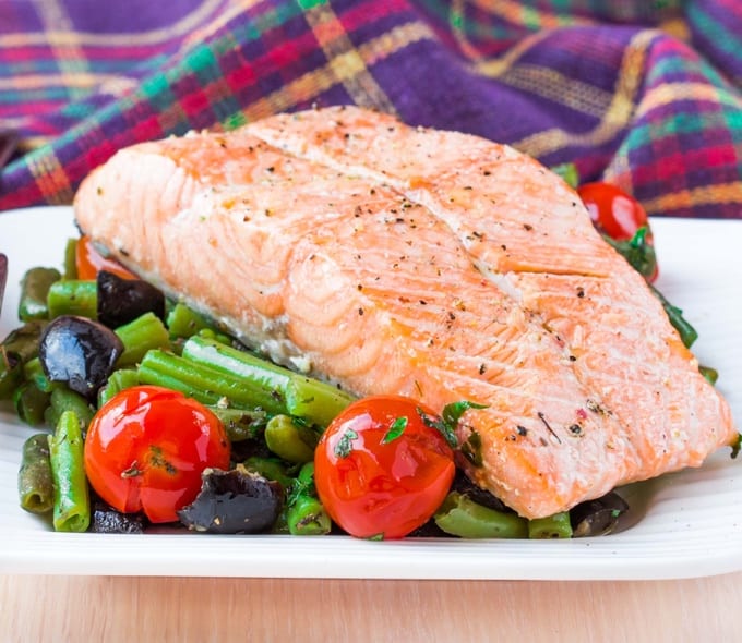 Salmon fillet on a bed of vegetables with colorful plaid napkins in the background.