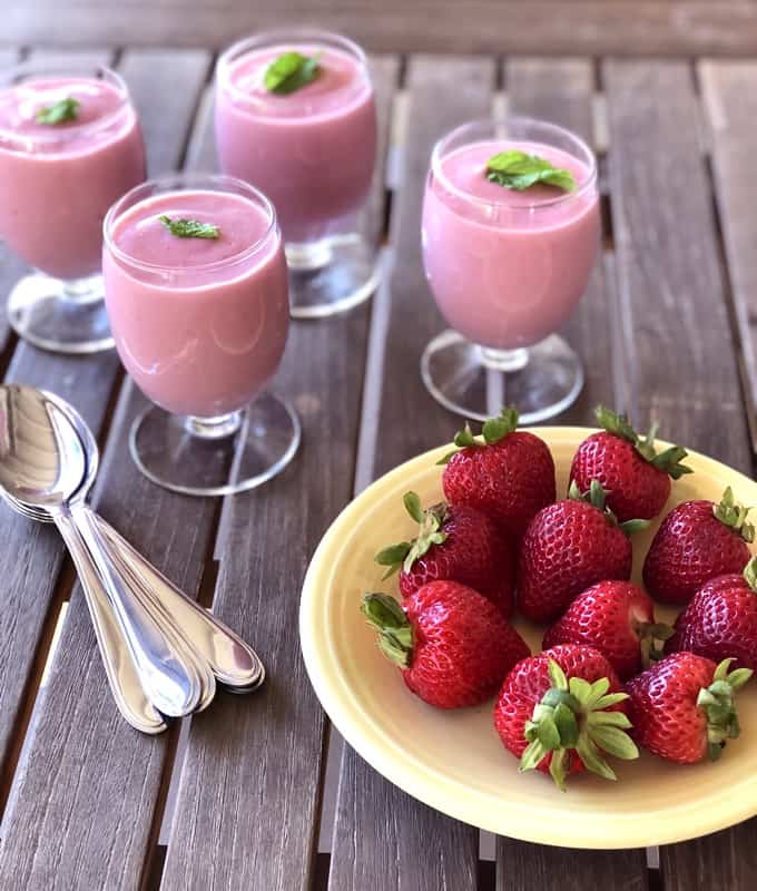 Four dessert glasses with strawberry mousse near plate of whole fresh strawberries.