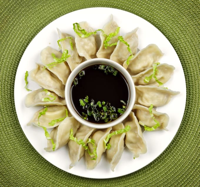Platter of vegetarian Chinese steamed dumplings with small bowl of soy dipping sauce.