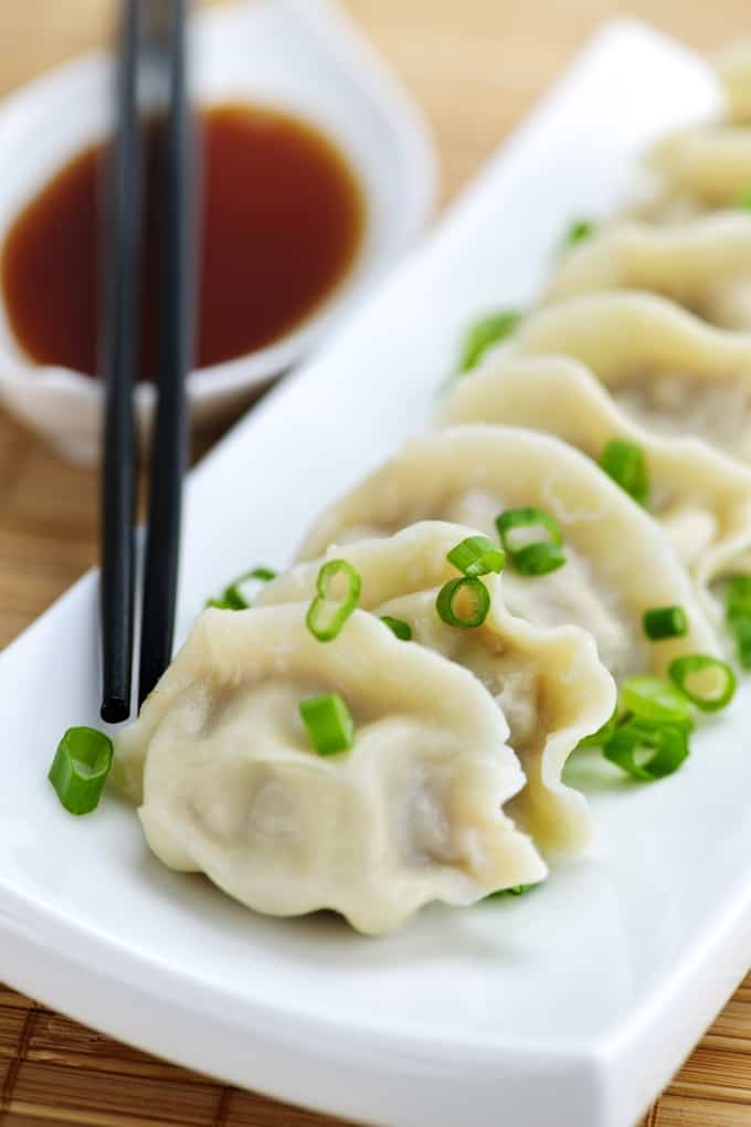 Steamed vegetarain dumplings on plate with bowl of soy dipping sauce and chopsticks.