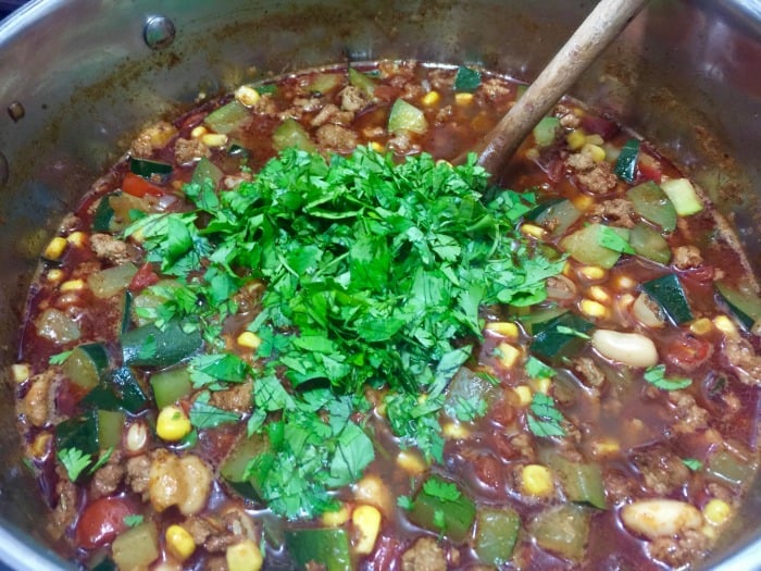 Stirring chopped cilantro into southwest ground turkey soup in large soup pot.