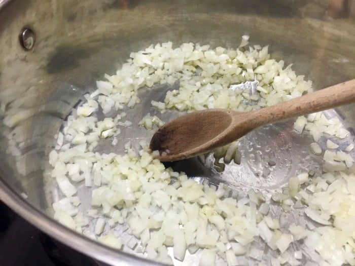 Cooking onion in stock pot with wooden spoon.