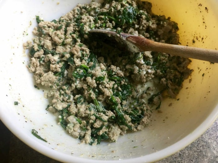 Mixing bowl with ground turkey, spinach and goat cheese and stirring with wooden spoon.