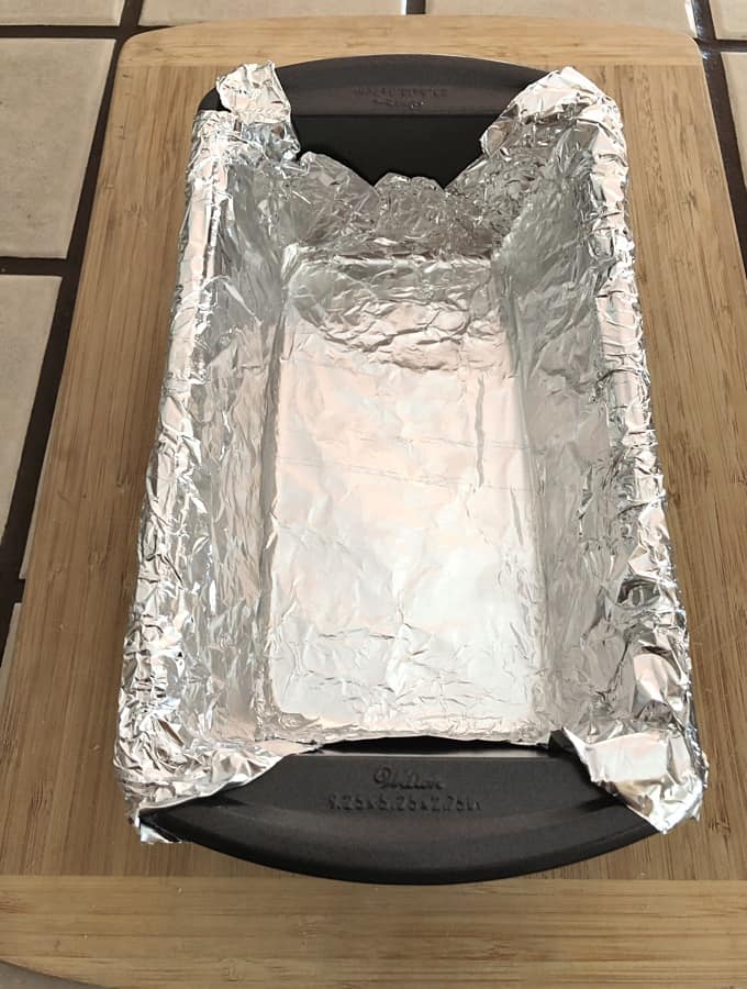 9x5-inch loaf pan lined with aluminum foil on wooden cutting board.