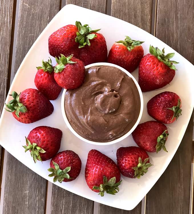 Brownie Batter Chocolate Hummus in bowl surrounded by plate of fresh strawberries.