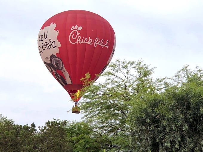 Red Chick-fil-A hot air balloon over some trees.