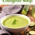 Creamy courgette soup in a white bowl with whole zucchini and zucchini slices scattered about.