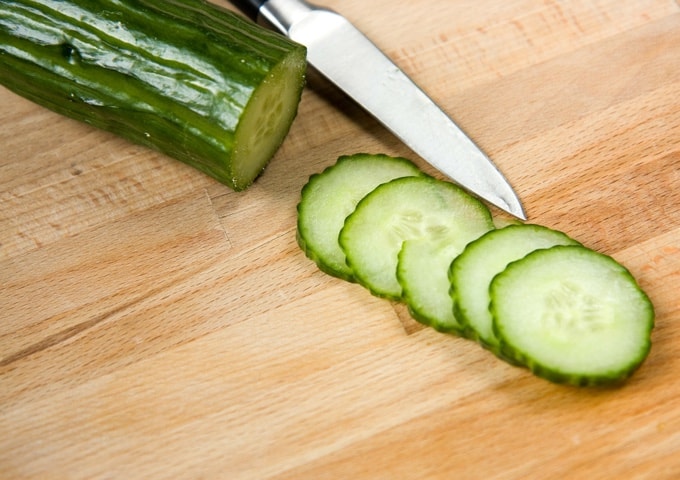 Fresh cut cucumber slices with knife on wood cutting board.