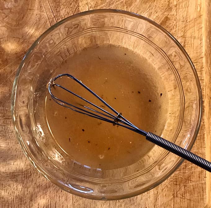 Whisking homemade salad dressing in small glass bowl.