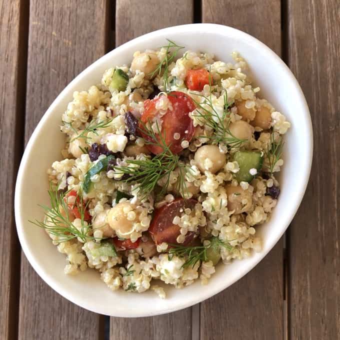 Vegetarian Greek Quinoa Salad topped with fresh dill in small white bowl on wooden table.