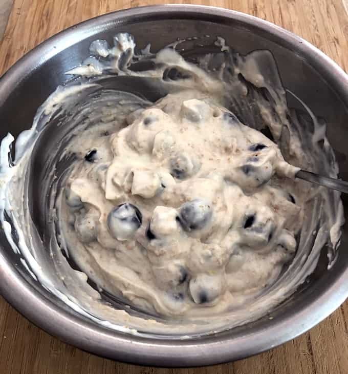 Adding blueberries and graham cracker crumbs to cheesecake yogurt mixture.