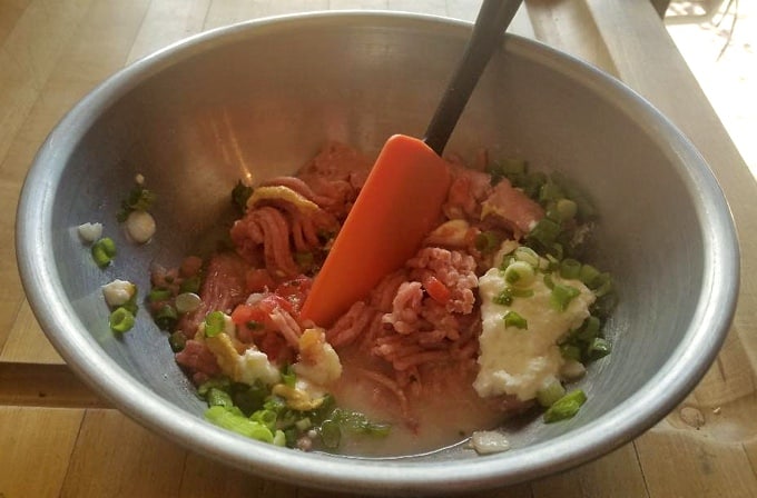 Mixing meatloaf ingredients with spatula in stainless steel bowl.