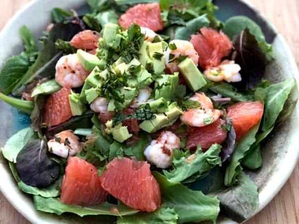 colorful composed salad of greens, shrimp and fresh pink grapefruit on potter plate set on light wooden tone background