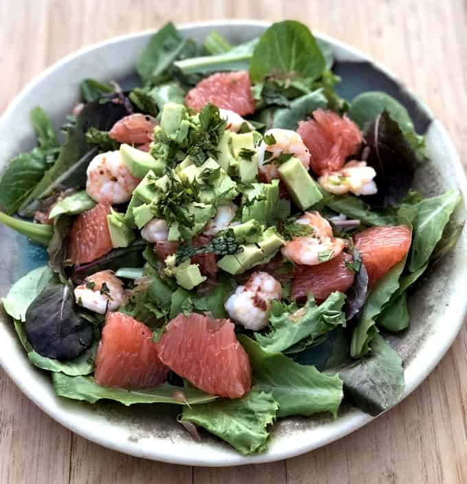 colorful composed salad of greens, shrimp and fresh pink grapefruit on potter plate set on light wooden tone background