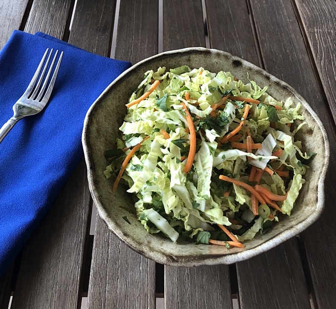 Spicy cabbage slaw in pottery bowl with blue cloth napkin and fork.