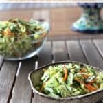 Spicy cabbage slaw in ceramic dish near larger glass bowl with cabbage slaw on wood table.