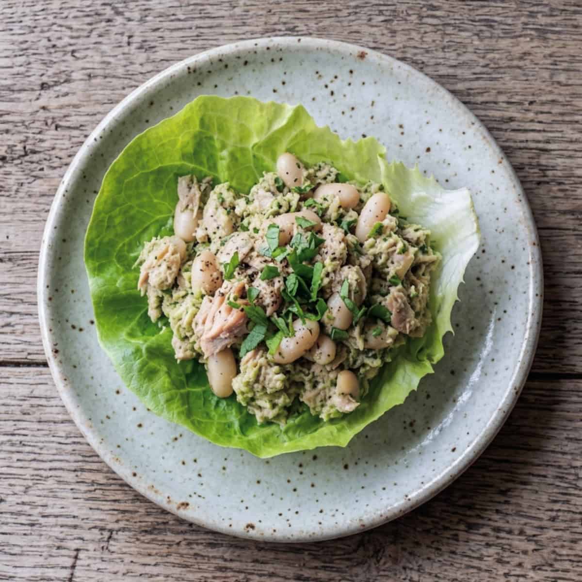 Summer tuna and white beans on butter lettuce leaf on small ceramic plate.