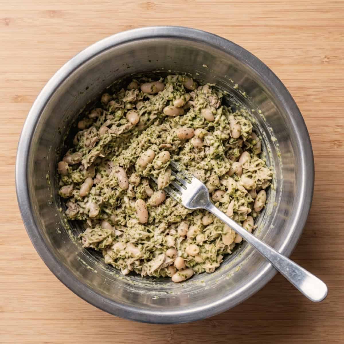 Mixing tuna and white beans in a mixing bowl with a fork.