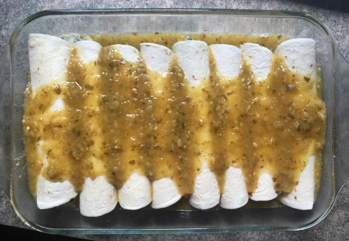 Rolled enchiladas in glass baking dish topped with tomatillo salsa.