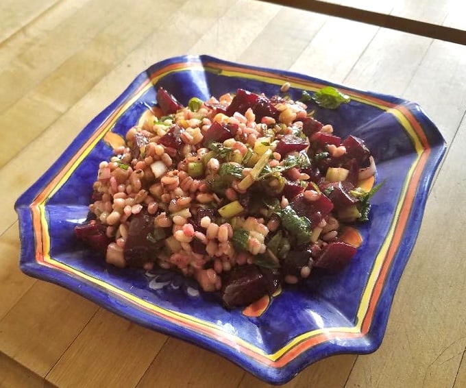 Barley beet salad in blue plate on wooden counter.