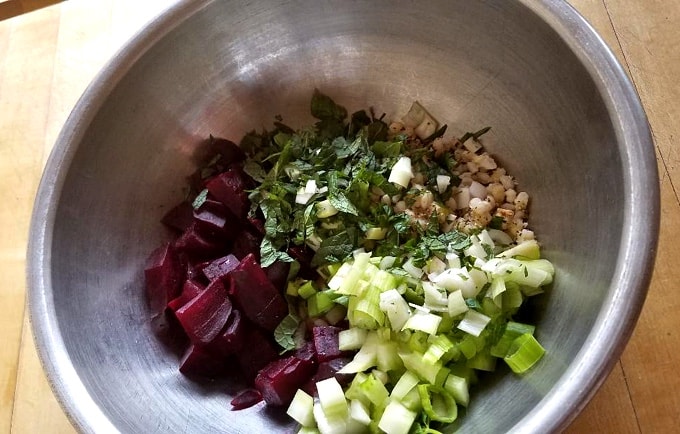 Chopped red beets, cooked barley, chopped celery, chopped green onion, chopped mint in stainless steel mixing bowl.
