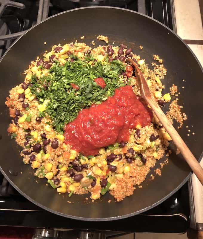 Stirring in chopped cilantro and salsa to Southwestern Quinoa Skillet with wooden spoon.