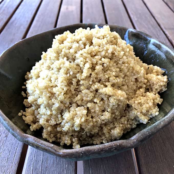 Plain cooked quinoa in green ceramic bowl on wooden table.