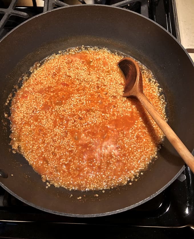 Quinoa cooked with salsa in skillet with wooden spoon.
