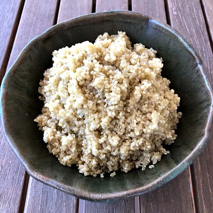 Plain cooked quinoa in green ceramic bowl on wood table.