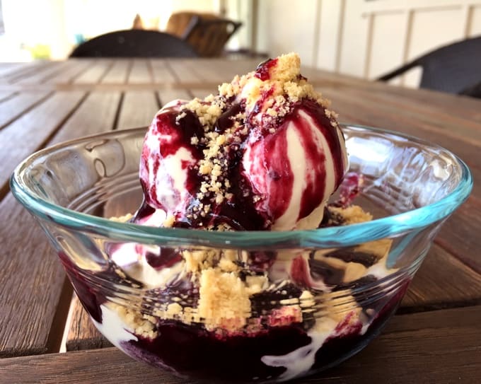 Blueberry pie sundae with vanilla frozen yogurt and crumbled shortbread finger cookies in small glass bowl.