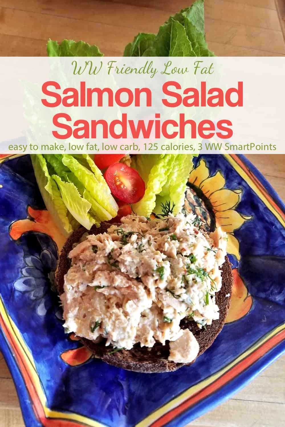 Open-face salmon salad sandwich on whole grain bread with romaine lettuce and cherry tomatoes on blue ceramic plate.